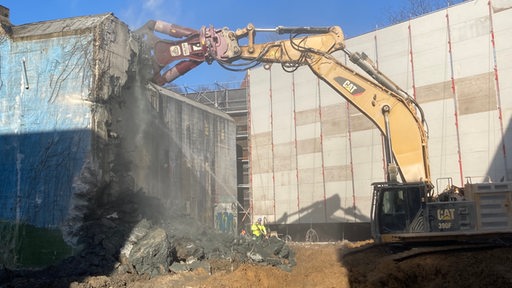 Ein Bagger mit einer Zange reißt eine Betonwand ein.