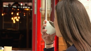 Eine Frau die aus einer weißen Tasse trinkt. 