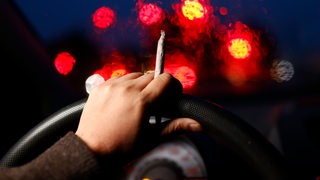 Ein Joint mit Tabak wird am Auto-Lenkrad gehalten