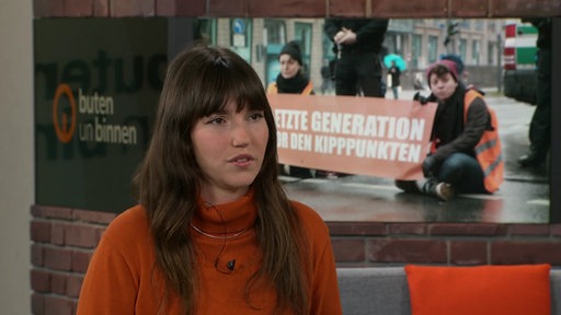 Eine Frau mit dunklen Haaren und orangenem Pullover im Studio von buten un binnen.