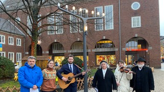 Mehrere Personen stehen unter einem großen Kerzenständer.