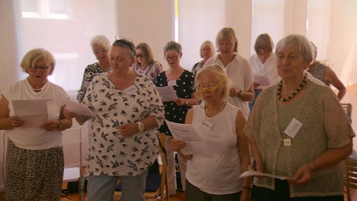 Mehrere Senioren singen zusammen im Chor und schauen auf einen Liedzettel.