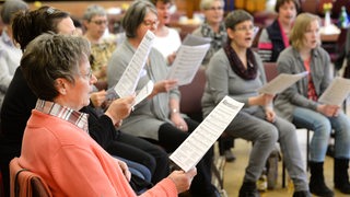 Mehrere Menschen mit Notenblättern singen im Chor.