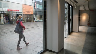 An einem leerstehenden Ladengeschäft in der Obernstraße geht eine Frau mit OP-Maske vorbei