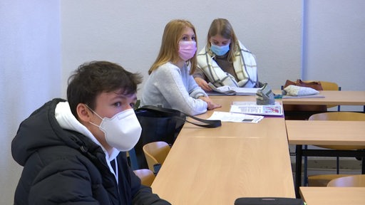 Drei Schüler mit Atemschutzmasken sitzen an einer Tischreihe