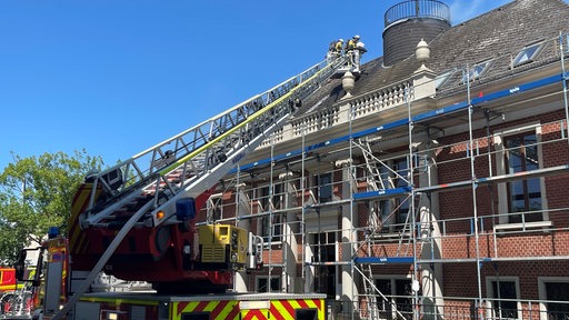 Ein Feuerwehrauto mit Drehleiter neben einem brennenden Dachstuhl.