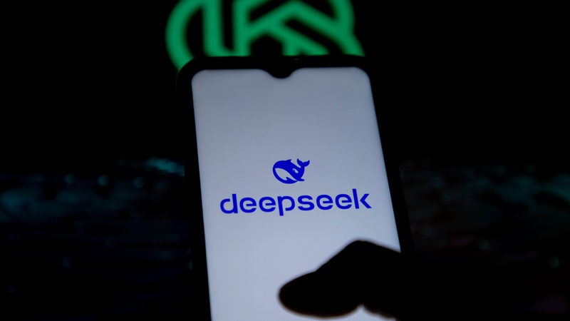 Fotomontage zeigt das "deepseek"-Logo auf einem Mobiltelefon vor dem Logo von Open AI im Hintergrund