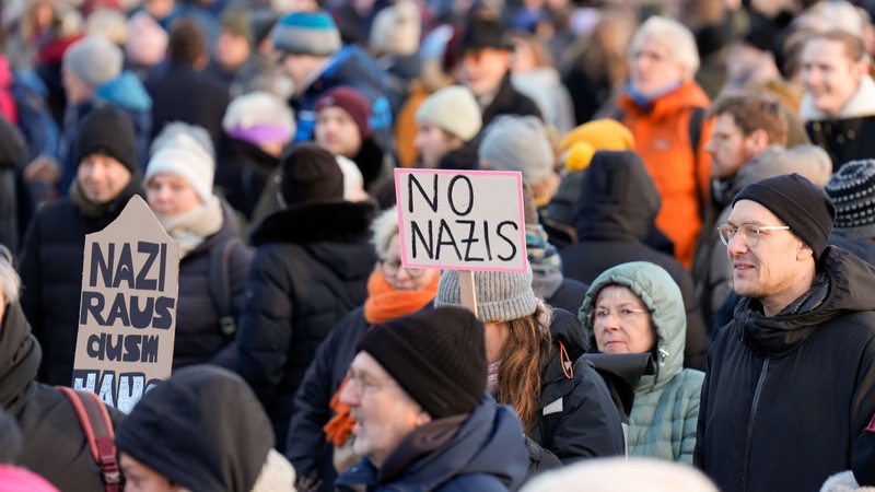 Mehrere Personen in einer Menschenmenge halten Schilder hoch.