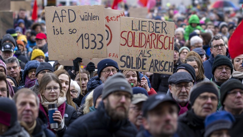 Mehrere Menschen halten bei einer Kundgebung bemalte Plakate in die Höhe.