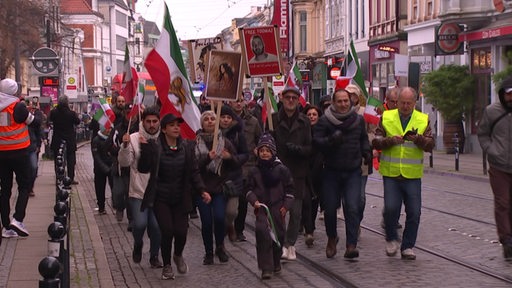 Personen demonstrieren im Bremer Viertel. Sie halten Iranflaggen in der Hand.