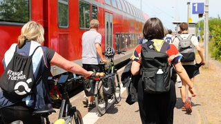 Fahrgäste laufen auf einem Bahnsteig neben einem Regionalexpress (Archivbild)