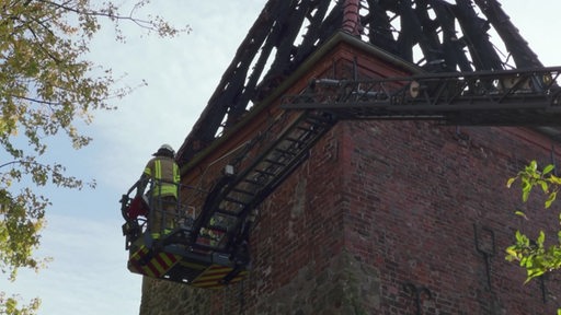 Ein Feuerwehrmann steht auf einer Drehleiter an einem Kirchturm.