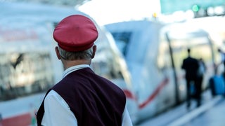 Ein Schaffner gibt ein Abfahrtszeichen für einen ICE auf einem Bahnsteig. 