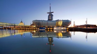 Beleuchtetes Klimahaus in Bremerhaven spiegelt sich bei Dämmerung im Wasser.