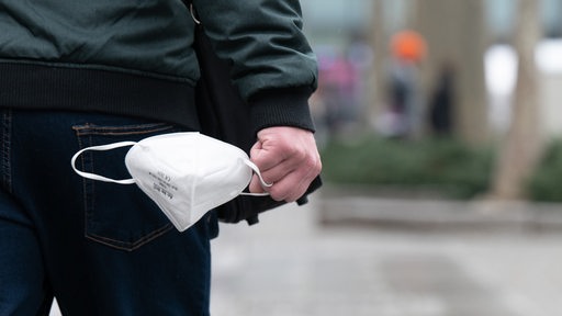 Ein Mann trägt auf einer Einkaufsstraße eine FFP-2-Maske in der Hand. 