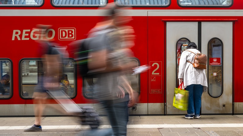 Reisende laufen in einem Bahnhof über einen Bahnsteig.