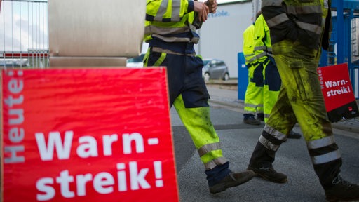 An einem Warnstreikschild gehen Hafenarbeiter vorbei