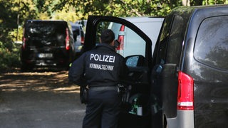 Eine Kriminaltechnikerin steht in der Nähe vom S-Bahnhof Hohenschönhausen neben Fahrzeugen der Polizei.