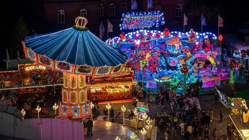 Die Beleuchtung mehrerer Fahrgeschäfte auf dem Freimarkt strahlt in der Nacht. Blick von oben aus der Luft.