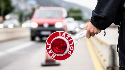 Ein Polizist hält auf einer Autobahn eine Kelle mit der Aufschrift "Halt Polizei" in der Hand. 