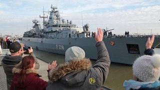 Menschen winken einem auslaufenden Schiff zu.