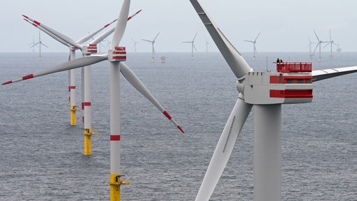 Zwei Techniker sind am 27.07.2017 auf einer Generatorgondel eines Windkraftrades (r) des Offshore-Windparks «Nordsee 1» in der Nordsee vor der ostfriesischen Insel Spiekeroog (Niedersachsen) mit der Inbetriebnahme beschäftigt.