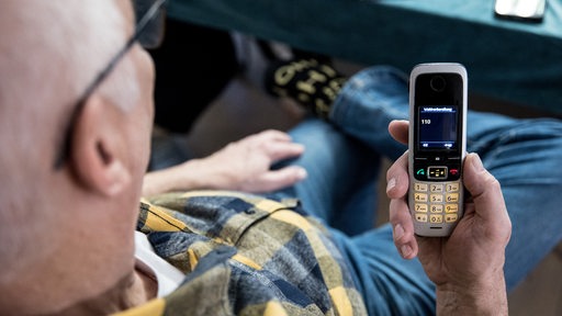 Ein älterer Mann hält ein Telefon in der Hand auf dem die 110 angezeigt wird.