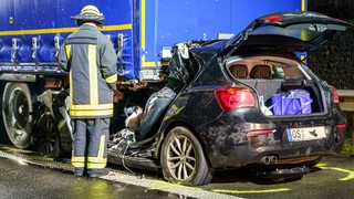 Ein Autowrack steht unter einem Lkw