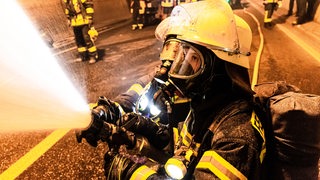 Feuerwehrleute halten einen Schlauch aus dem Wasser spritzt