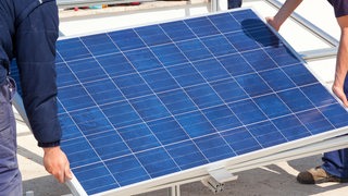 Zwei Menschen tragen ein Solarmodul