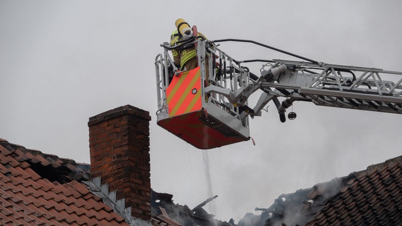 Einsatzkräfte der Feuerwehr löschen einen Brand von einer Drehleiter aus