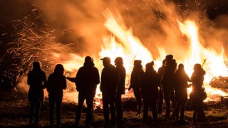 Mehrere Menschen stehen vor einem großen Feuer.