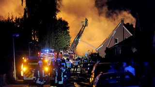 Feuerwehrleute löschen von einer Drehleiter aus ein Feuer auf einem Fabrikgelände.