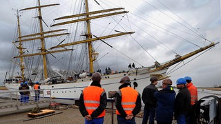 Werftarbeiter schauen auf ein großes Segelschiff