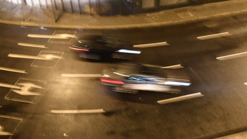 Zwei Autos rasen über eine Straße. Die Autos sind durch Bewegungsunschärfe verwischt dargestellt. Es handelt sich um ein Symboldbild.