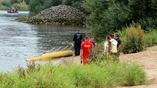 Rettungskräfte der DLRG und Polizisten stehen am Ufer der Weser. 