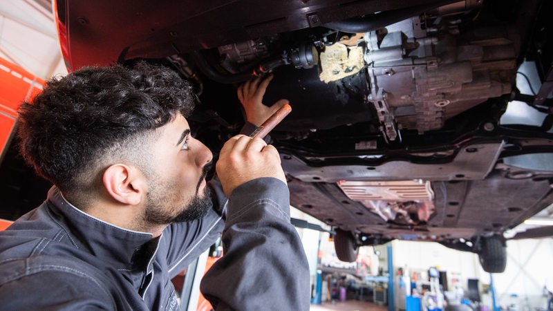 Ein junger Mann untersucht den Unterboden eines Autos.