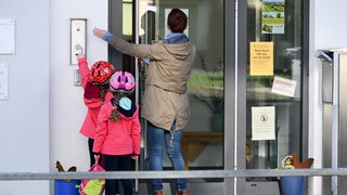 Eine Mutter mit zwei Kindern klingelt an einer Tür zu einer Kita.