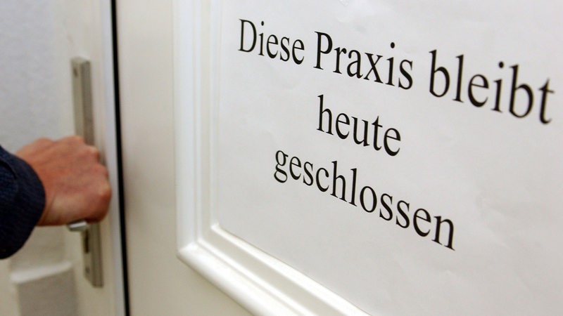 An der Eingangstür einer Arztpraxis hängt ein Hinweiszettel mit der Aufschrift: "Diese Praxis bleibt heute geschlossen". 