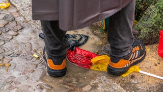 Ein Demonstrant steht mit den Füßen auf einer Deutschlandflagge, die auf dem Boden in einer dreckigen Pfütze liegt. (Archivbild)