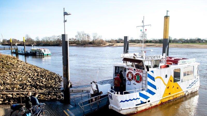 Mehrere Menschen betreten bei sonnigem Wetter die kleine Sielwallfähre an der Weser, um vom Osterdeich zum Stadtwerder überzusetzen.