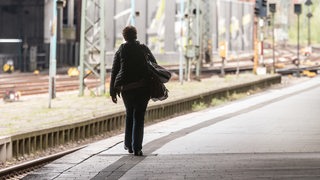 Eine Frau wartet an einem Bahnsteig auf einen Zug.