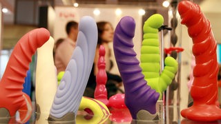 Verschiedene bunte Dildos werden auf einer Erotikmesse präsentiert.