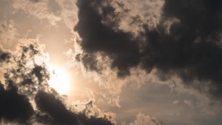 Dunkle Wolken ziehen vor der Sonne über den Himmel.