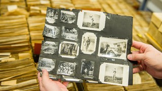 Ein Archivar hält im Archiv des DRK-Suchdienstes eine Karteikarte mit mehreren Fotos in den Händen.