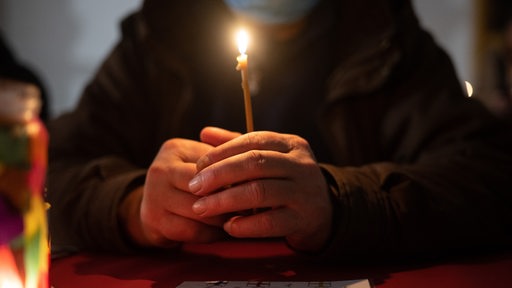 Ein Rentner hält eine Kerze in der Hand und sitzt alleine am Tisch