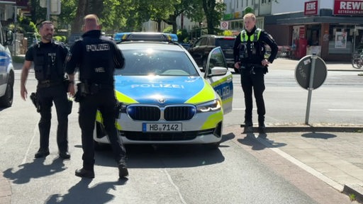 Mehrere Polizisten vor einem Polizeiwagen vor dem REWE in der Kuhlenkampffallee