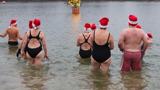 Männer und Frauen mit Nikolausmützen gehen bei Minusgraden in einen See (Archivbild) 