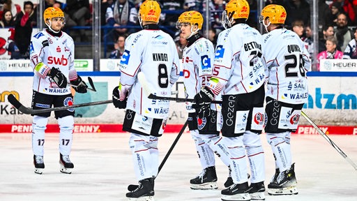 Eishockey-Spieler der Fischtown Pinguins stehen auf dem Eis zusammen und besprechen sich.