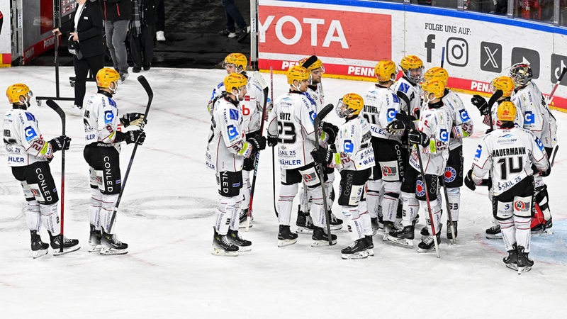 Die Eishockey-Spieler der Fischtown Pinguins aus Bremerhaven stehen nach dem Spiel auf dem Eis und klatschen sich ab.